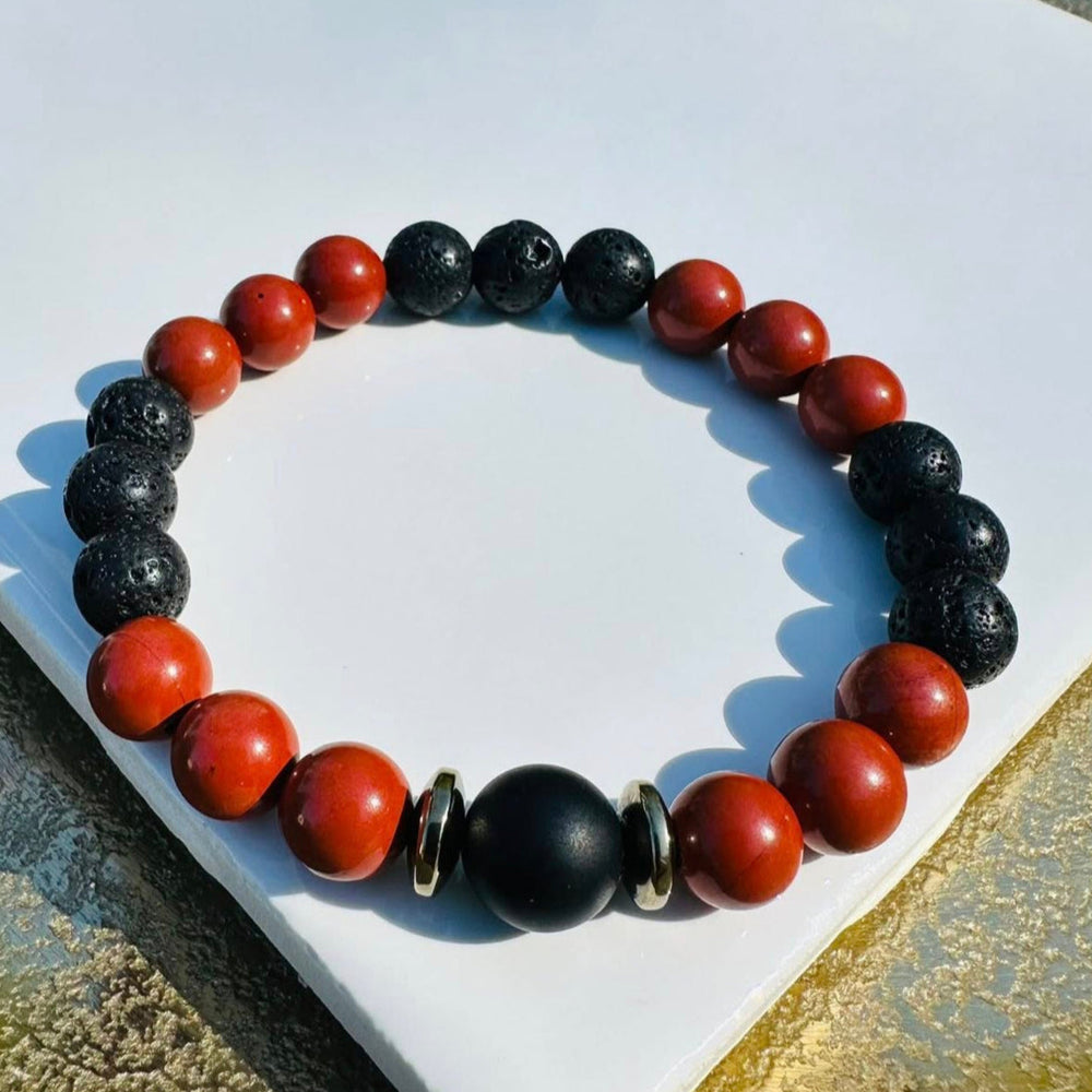 A bracelet of contrast and calm—porous black lava beads meet smooth reddish-brown warmth, centered by a matte black bead and two metallic rings. Grounded, earthy, and quietly powerful.