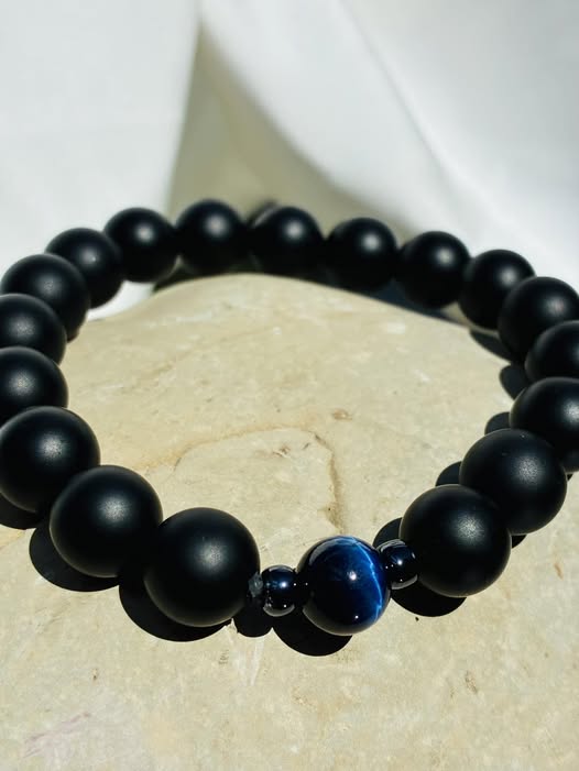 A matte black bracelet with a single glossy dark blue bead at its center, flanked by two shiny black accents—minimalist, bold, and quietly refined